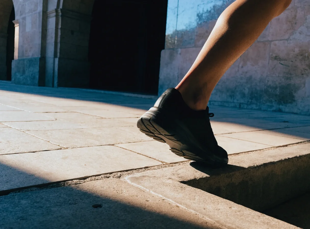 Piernas de un adulto con calzado de paseo entrando en una acera en sombra con luz cálida lateral